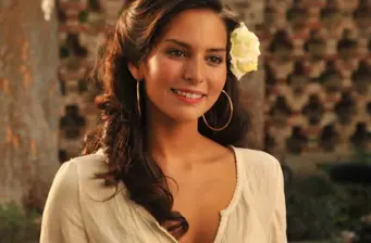 Genesis Rodriguez smiles with flower in hair and hoop earrings