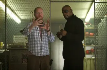 Two men in casual and formal wear in storage room, one gesturing