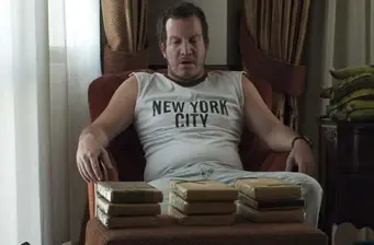 Man in sleeveless New York City shirt seated with three stacks of bricks