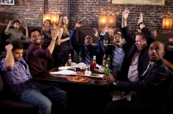 Group of men cheering around table with drinks and pizza