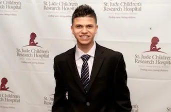 Young man in suit and tie stands in front of St. Jude banner