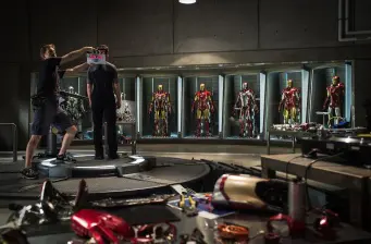 Iron Man suits displayed in workshop with crew adjusting clapperboard