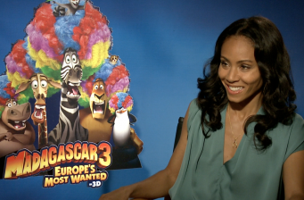 Jada Pinkett-Smith sitting smiling near Madagascar 3 poster
