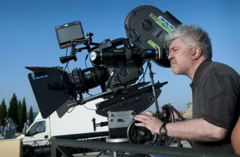 man operating film camera mounted on tripod outdoors