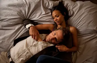 Zoe Saldana and man lying on bed in close embrace