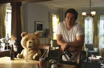 man in white shirt sits with talking teddy bear at kitchen table