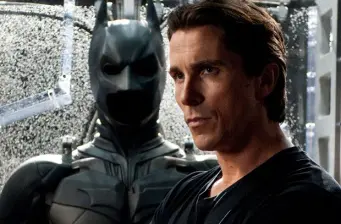 Batman suit behind man in black shirt, intense look