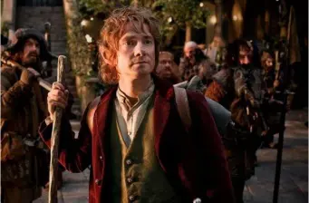 Bilbo Baggins holds walking stick outdoors, surrounded by medieval figures