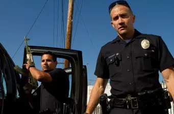 Two police officers, one armed, standing near a car door