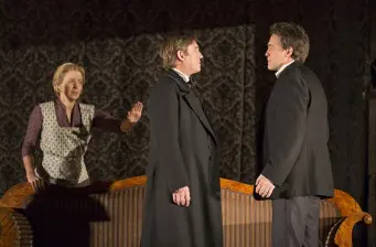 Two men in suits face off as woman gestures behind them on stage