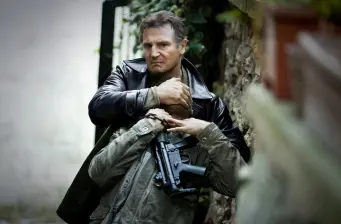 Liam Neeson grabbing a man holding a gun in action scene