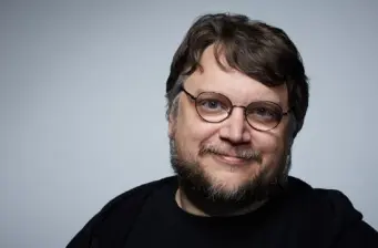 Headshot of Guillermo Del Toro smiling against a gray background