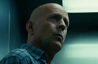 bald man in blue shirt looks up in dim light