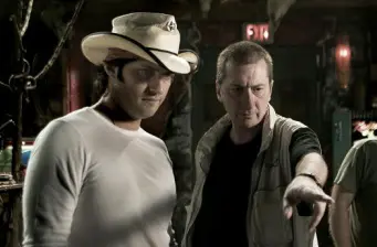 Robert Rodriguez and another man discuss on film set, man wears white cowboy hat