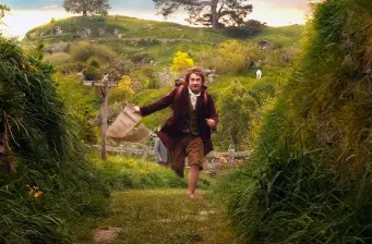 Bilbo Baggins runs barefoot holding bag in green countryside