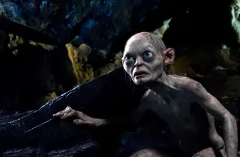 Gollum crouches in dark cave, eyes wide and alert