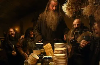 Gandalf and dwarves share a feast with plates and bowls stacked high