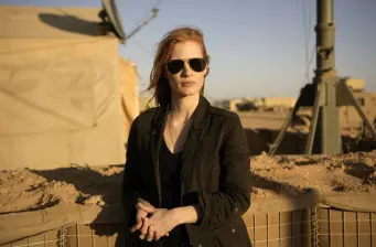 Woman wearing sunglasses and black jacket outside near military equipment