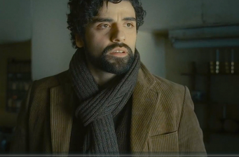 Oscar Isaac in brown jacket and scarf looking offscreen in film scene