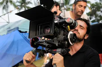 man peering through movie camera viewfinder on outdoor set