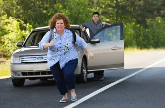 Woman running on road while man stands by open car door