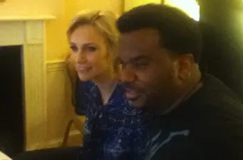 A woman and man sit indoors smiling, engaged in conversation