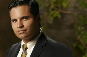 Michael Peña headshot wearing suit and striped tie
