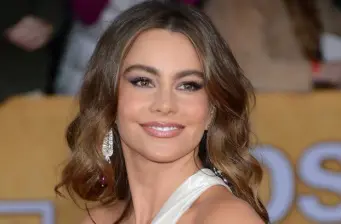 Sofia Vergara smiling in headshot with earrings and wavy hair