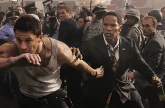 man in tank top restrained by suited man during chaotic scene