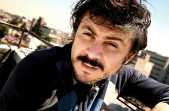 man with mustache and dark hair leans on railing outdoors