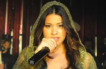Gina Rodriguez at event, holding microphone, focused while speaking
Gina Rodriguez speaks into microphone wearing hooded garment