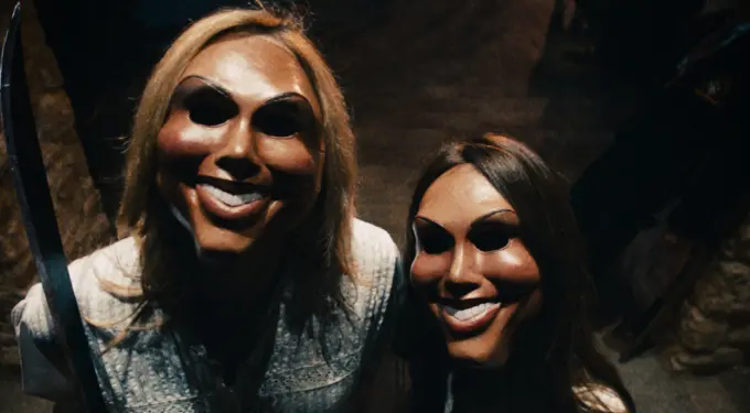 Two people wearing creepy masks, one holding a machete, in dark setting