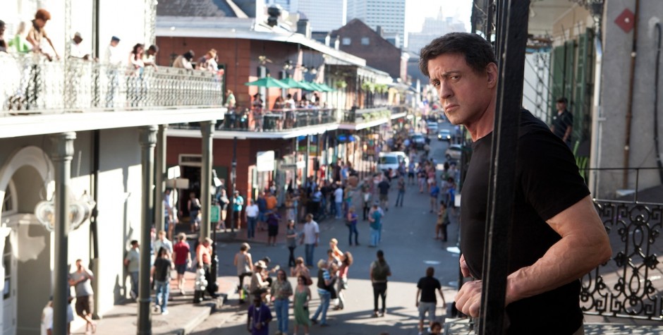 Man in black shirt leans on balcony overlooking busy street