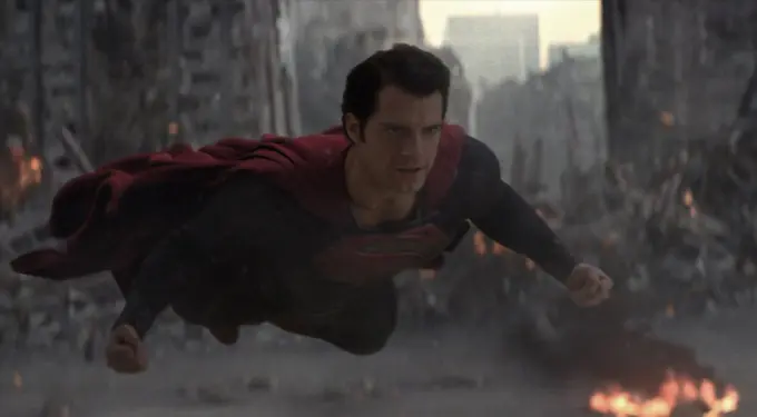 Superman in costume flies over destroyed city with smoke and fire