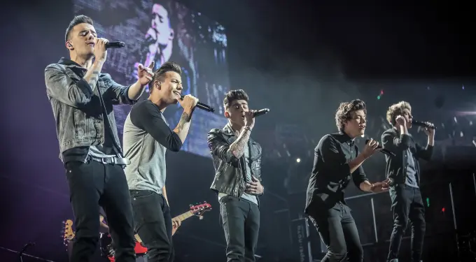 Five male singers performing on stage with microphones in hand