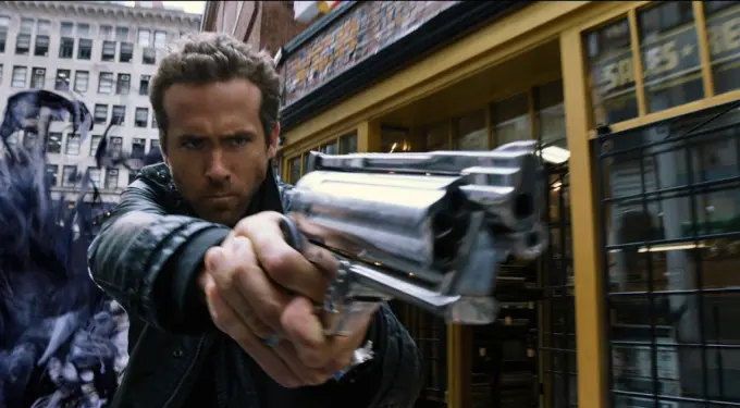 Ryan Gosling aims a gun with shadowy figure behind in city street