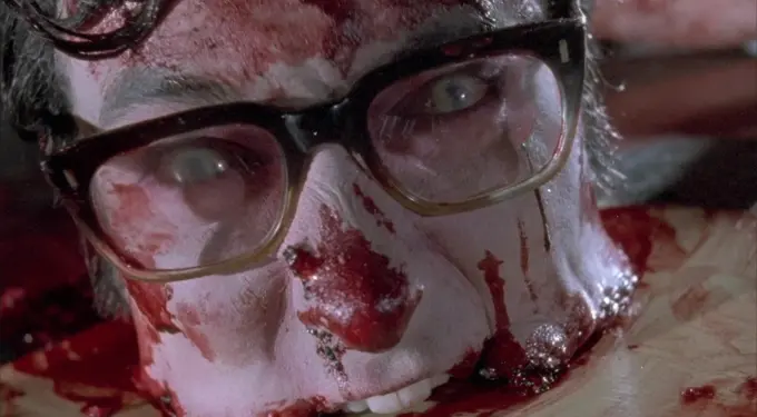 Close-up of bloodied man with glasses and white face paint lying down