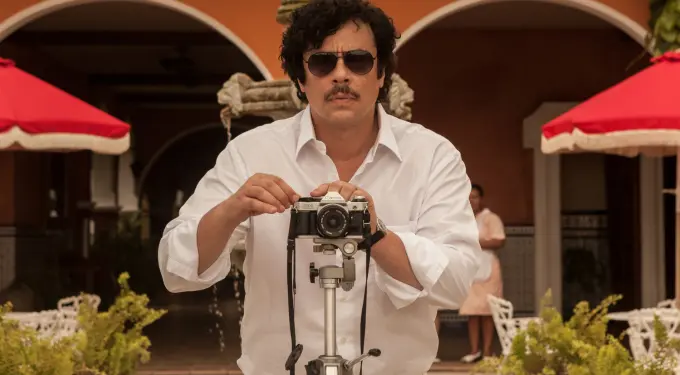 Benicio del Toro as Pablo Escobar adjusts camera on tripod outdoors
