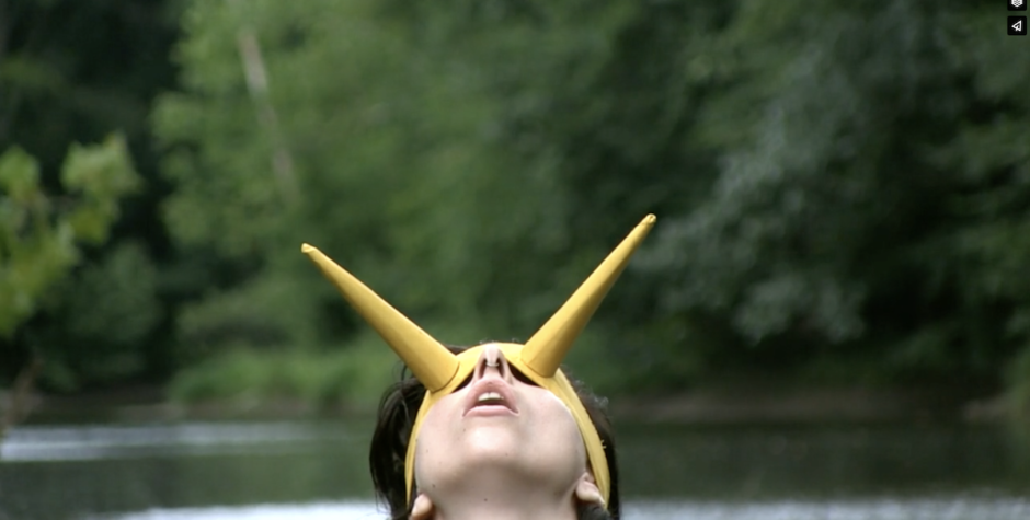 Lady Gaga in a striking yellow horned mask, looking upward near a river.
Lady Gaga wearing a yellow horned headpiece outdoors near water