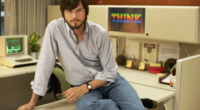Ashton Kutcher as Steve Jobs sitting on desk in early Apple office