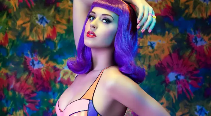 Katy Perry with purple hair posing in colorful outfit against floral background