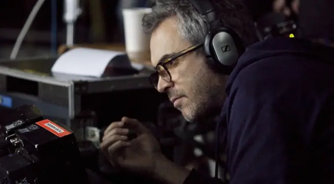 Alfonso Cuarón wearing headphones, closely inspecting camera gear