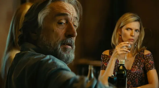 man with gray beard looks back, woman in floral dress holds wine glass