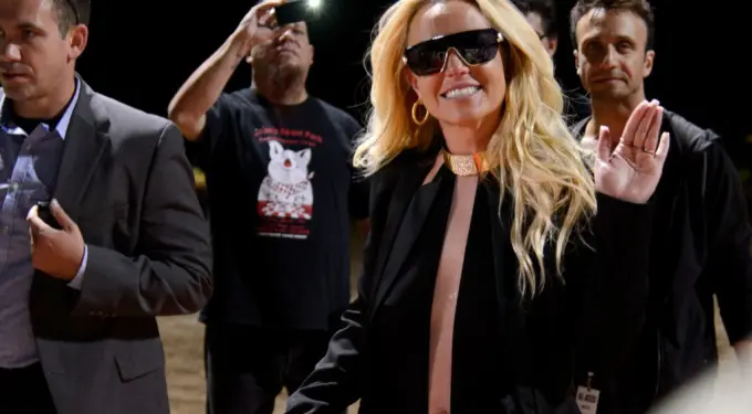 Britney Spears waves and smiles wearing black outfit and sunglasses