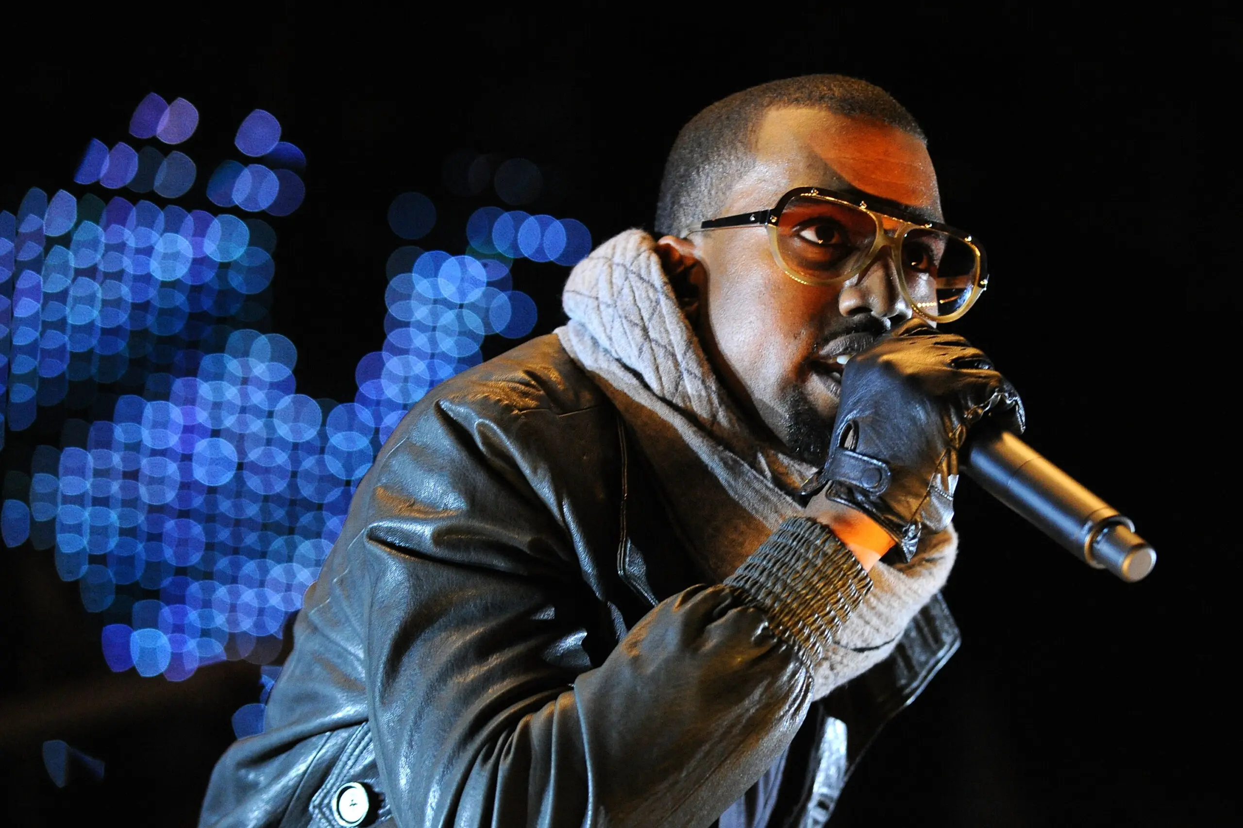 Kanye West performing live on stage wearing leather jacket and glasses