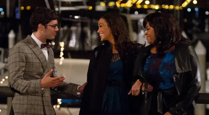 Man talks to two women smiling by boats at night