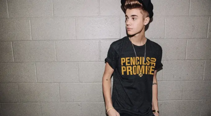 Justin Bieber in Pencils of Promise shirt and cap against gray wall