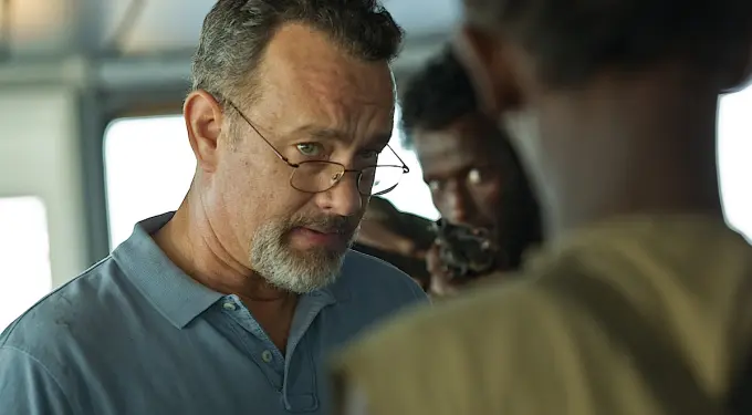 Tom Hanks in blue shirt faces man with gun in tense scene