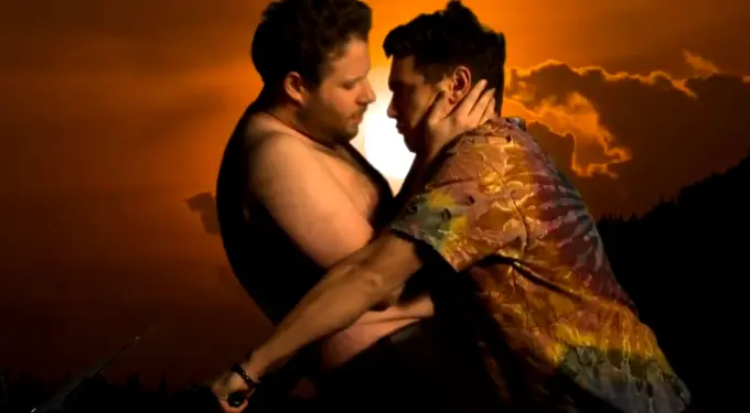 Seth Rogen and James Franco embrace closely with sunset behind