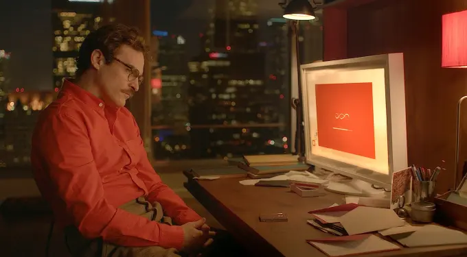 Joaquin Phoenix in red shirt sitting at desk with computer